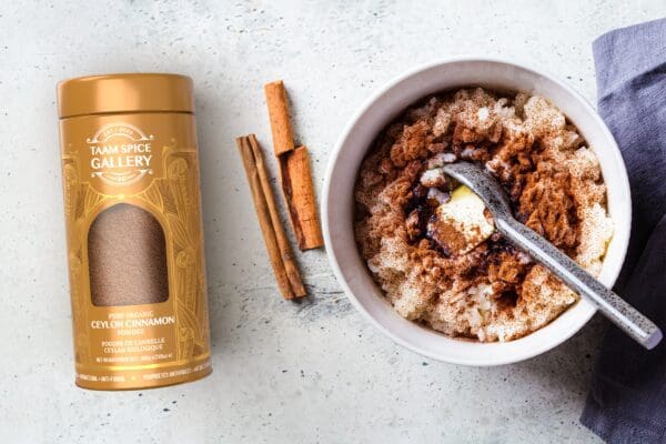 A bowl of rice pudding next to a jar of cinnamon.