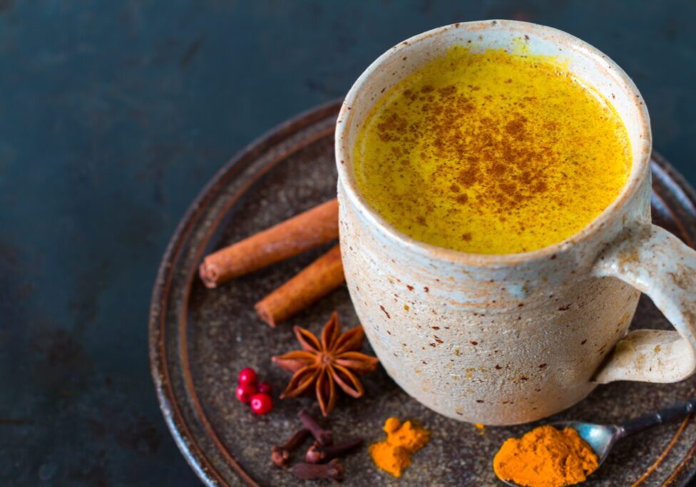 Turmeric milk in a cup with spices on the side.